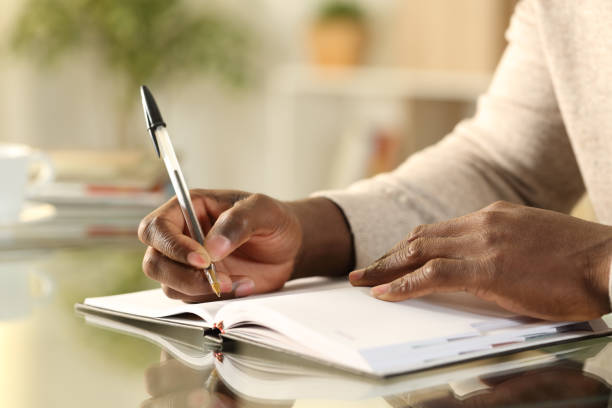 Close up of a black man hands writing reminder on paper agenda on a desk at home